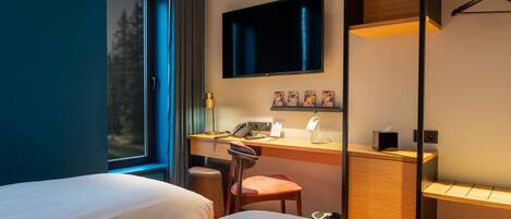 A hotel room with two beds, a desk with a chair, a TV, and a window with curtains.