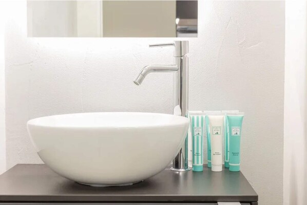 A bathroom with a white sink, a modern faucet, and three toiletry bottles.