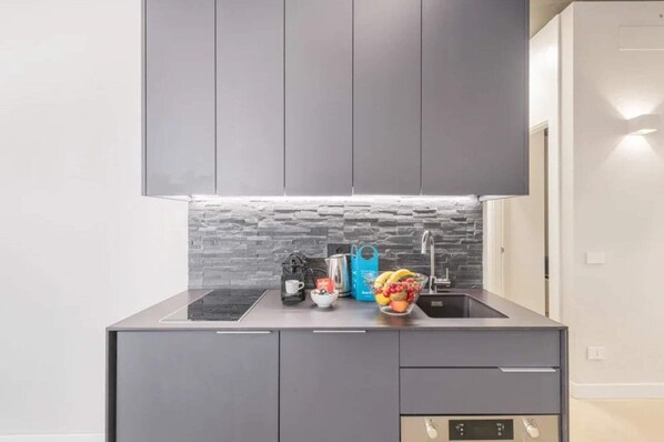 A modern kitchen with grey cabinets, a black countertop, and a stone backsplash.