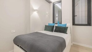Un dormitorio con cama, almohadas, una mesita de noche, un espejo y una ventana.