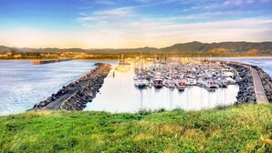 Un puerto deportivo con numerosas embarcaciones amarradas, rodeado por un rompeolas rocoso y una orilla cubierta de césped.