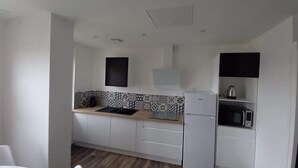 A compact kitchen with white cabinets, a wooden countertop, a sink, a microwave, and a kettle. - Brand new house with all comforts (Lucey)
