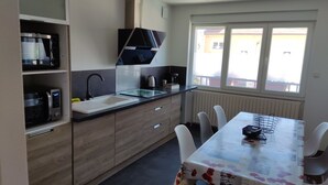 A modern kitchen with a built-in oven, a black range hood, a white sink, and a dining area with a table and chairs. - Brand new house with all comforts (Lucey)