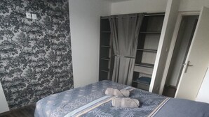 A bedroom with a patterned bedspread, a wooden floor, and a wardrobe with a mirror. - Brand new house with all comforts (Lucey)