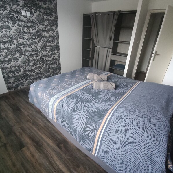 A bedroom with a patterned bedspread, a wooden floor, and a wardrobe with a mirror. - Brand-new house with all the amenities (Lucey)