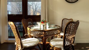 A dining area with a round table and wicker chairs, a wall clock, and a window with a view of trees and buildings. - One bedroom balcony apartment with allocated parking close to Gunwharf Quays (Portsmouth)