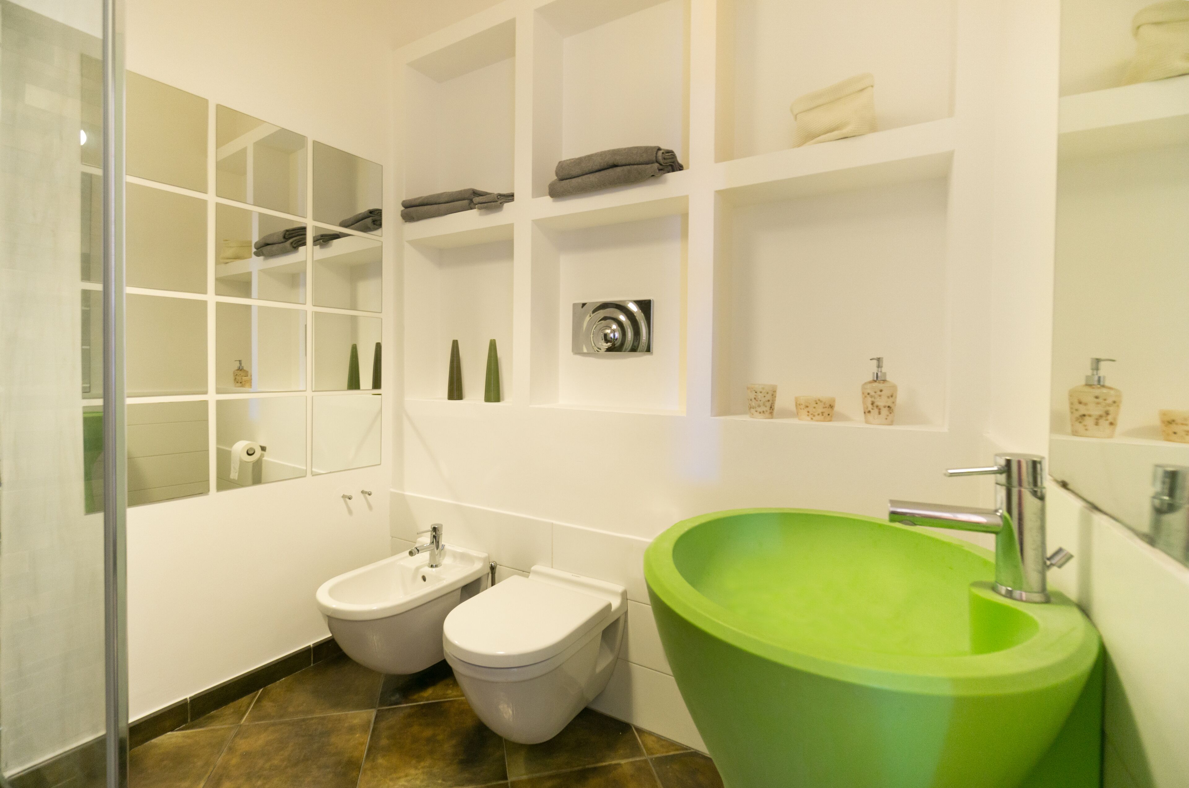 A modern bathroom with a green sink, two bidets, a white bathtub, and a glass shower enclosure.