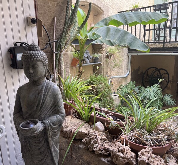 A statue of a figure holding a bowl, surrounded by potted plants and rocks. - Chambre Zen (AUTIGNAC)