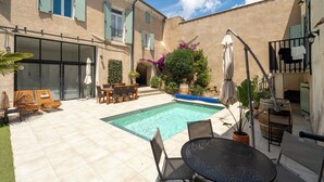 A pool area with a tiled deck, outdoor furniture, and a building with shutters. - Chambre Zen (AUTIGNAC)