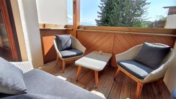A wooden deck with two wicker chairs and a small table, overlooking a forested area.