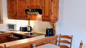 A kitchen with wooden cabinets, a microwave, a toaster, and a coffee maker. There is a table with a tablecloth and four chairs.