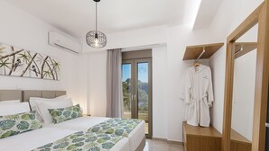 A bedroom with a bed, a wardrobe, a robe, and a view through a glass door. - Koin Villa Sunset,  With Heated Pool & Whirlpool (Perama, Rethymno)