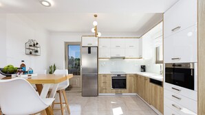 A modern kitchen with white cabinets, a stainless steel refrigerator, and a wooden dining table with white chairs. - Koin Villa Sunset,  With Heated Pool & Whirlpool (Perama, Rethymno)