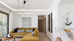 A modern living room with a sectional sofa, a round coffee table, and a dining area with white chairs and a wooden table. - Koin Villa Sunset,  With Heated Pool & Whirlpool (Perama, Rethymno)