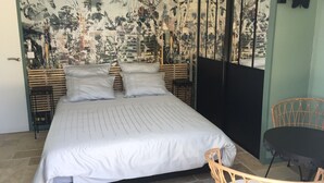 Quarto com uma cama grande, uma mesinha e uma cadeira.