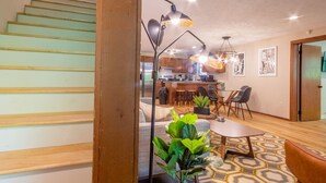 A modern kitchen with wooden cabinets and a central island, a dining area with a round table and chairs, and a staircase with wooden steps. - THE DOGWOOD @ DOLLYS DRIVE * Wifi Grill Woods Mtns (Sevierville)
