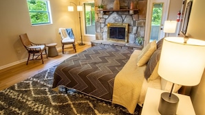 A bedroom with a stone fireplace, two chairs, a bed with a patterned bedspread, and a nightstand with a lamp. - THE DOGWOOD @ DOLLYS DRIVE * Wifi Grill Woods Mtns (Sevierville)