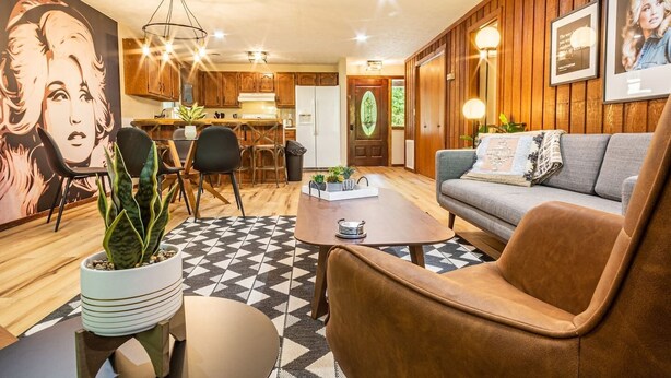 A modern living room with a brown leather sofa, a coffee table, and a dining area with wooden cabinets and chairs. - THE IRIS @ DOLLYS DRIVE * Wifi Grill Woods Mtns (Sevierville)
