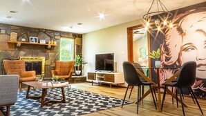 A modern living room with a stone accent wall, a fireplace, a large TV, and a dining area with chairs and a table. - THE IRIS @ DOLLYS DRIVE * Wifi Grill Woods Mtns (Sevierville)