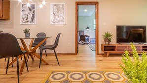 A modern living room with a dining area, wooden flooring, a TV, and framed artwork on the walls. - THE IRIS @ DOLLYS DRIVE * Wifi Grill Woods Mtns (Sevierville)