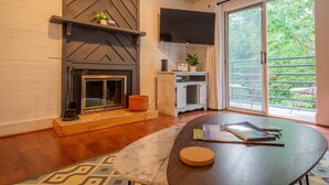 Een moderne woonkamer met een open haard, een flatscreen televisie en een grote schuifpui naar een balkon.