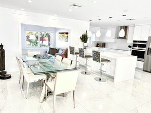Une cuisine moderne avec des meubles blancs, des appareils en acier inoxydable et des luminaires suspendus.