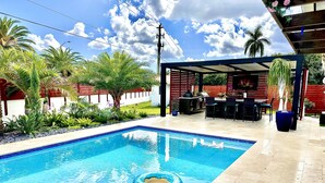 A swimming pool with a starfish float, surrounded by a patio area with outdoor furniture and a barbecue grill. - Luxury heated salt water pool, Grill BBQ Serenity Oasis  (Miami)