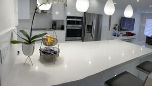 A modern kitchen with white cabinetry, stainless steel appliances, and pendant lighting. - Luxury heated salt water pool, Grill BBQ Serenity Oasis  (Miami)
