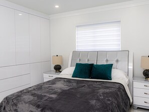 Une chambre à coucher moderne avec un lit, des tables de chevet et une fenêtre avec des stores.