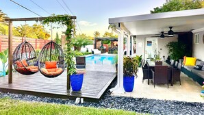 A poolside area with hanging chairs, a dining set, and potted plants. - Luxury heated salt water pool, Grill BBQ Serenity Oasis  (Miami)