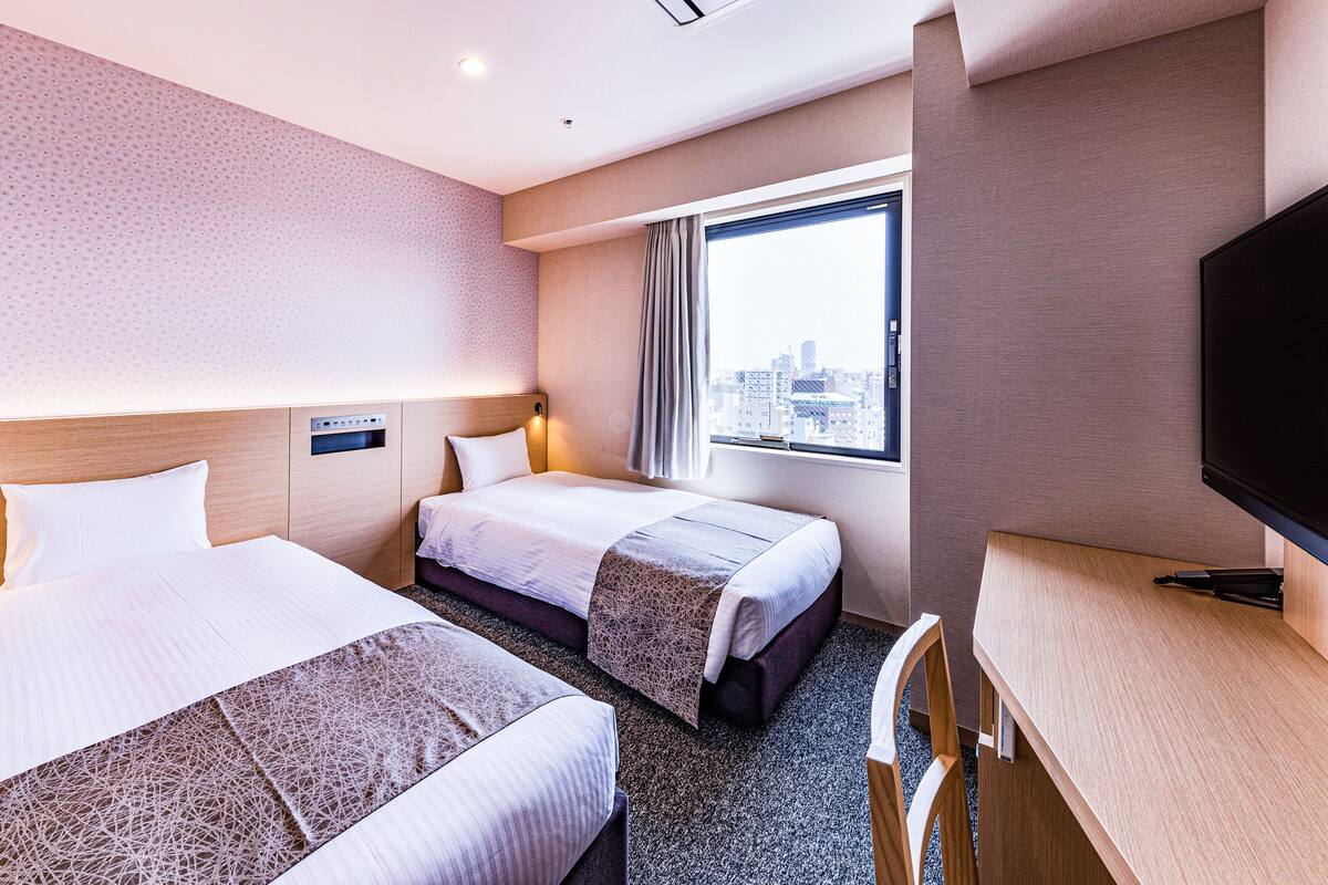 Een hotelkamer met twee bedden, een televisie, een bureau en een raam met uitzicht over de stad.