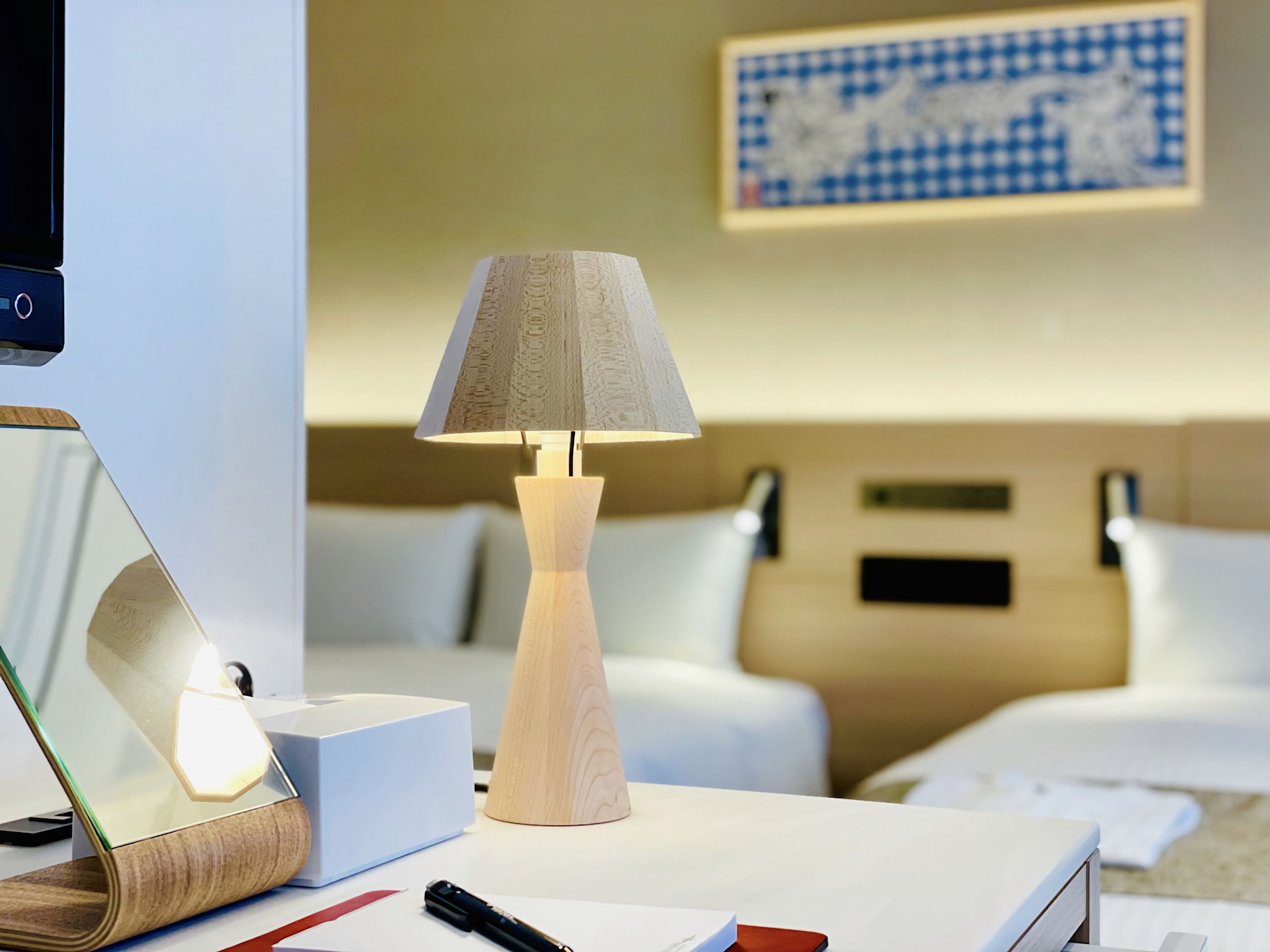 A hotel room with a bedside table, a lamp, a mirror, and a bed.