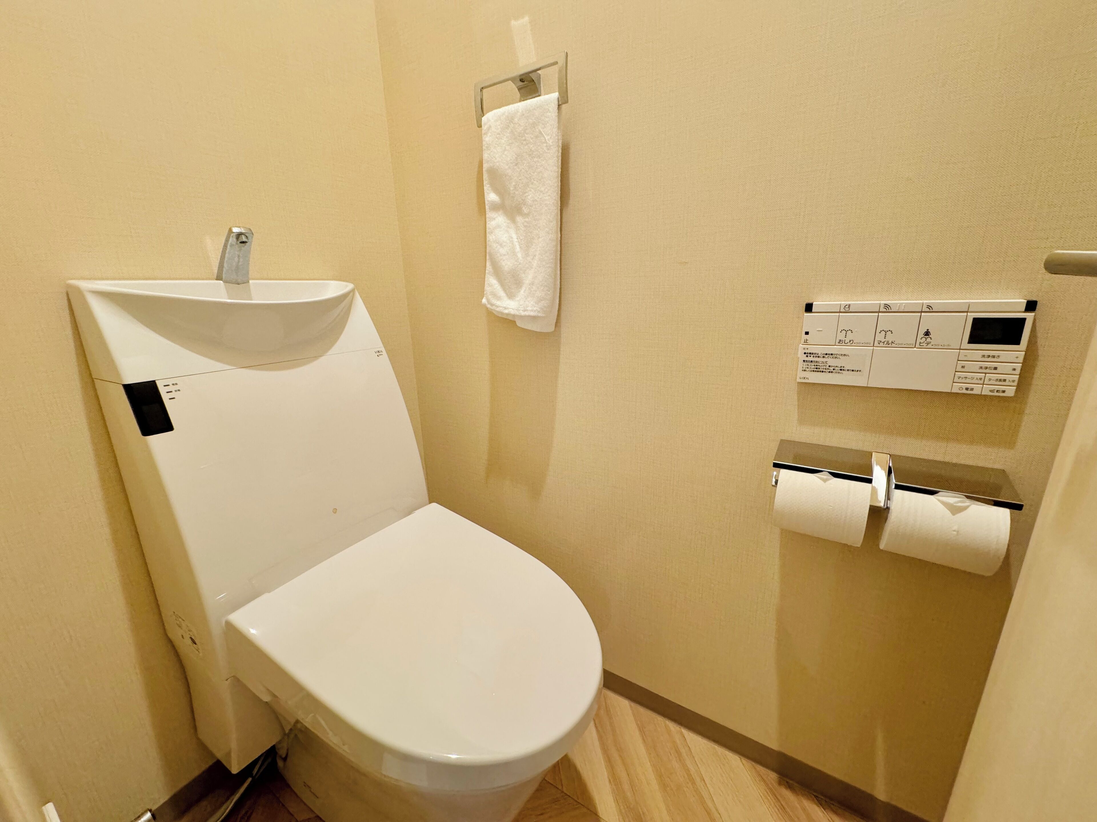 A small, compact bathroom with a white toilet, a sink, and a toilet paper holder.
