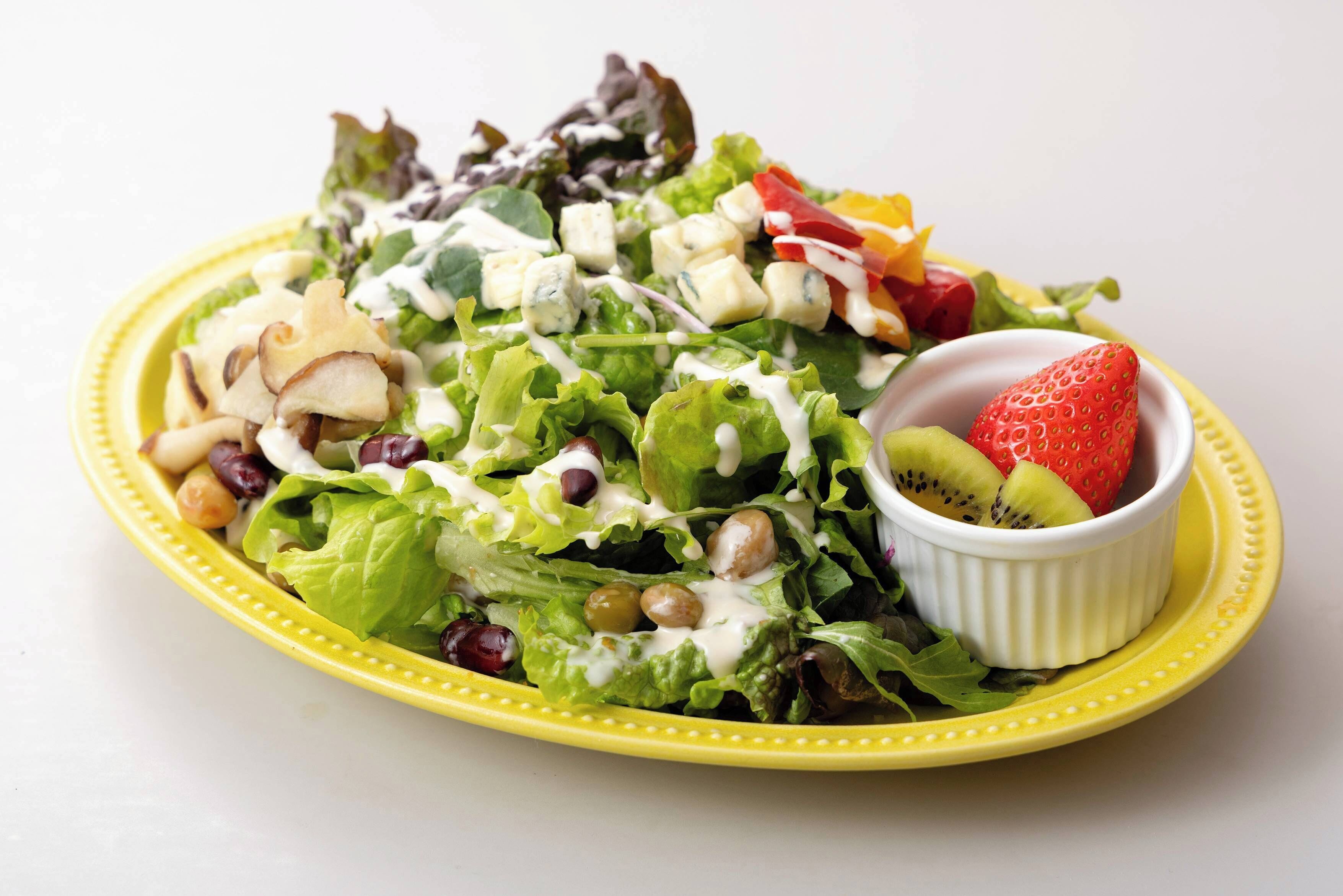 A salad with various ingredients and a small bowl of fruit on a yellow plate.