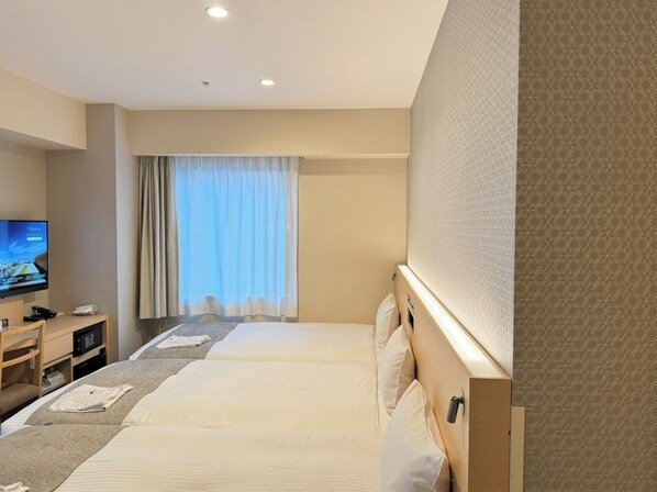 A hotel room with two beds, a TV, a desk with a computer, and a window with curtains.