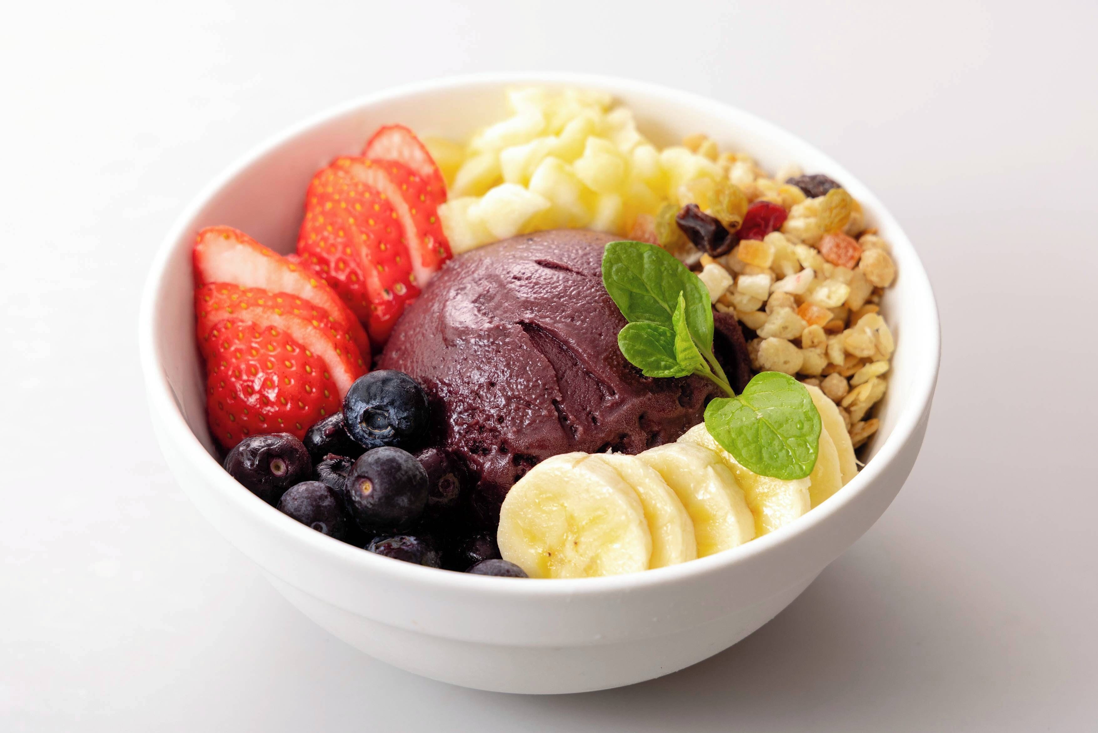 Un tazón de helado con fresas, arándanos, rodajas de plátano y granola.