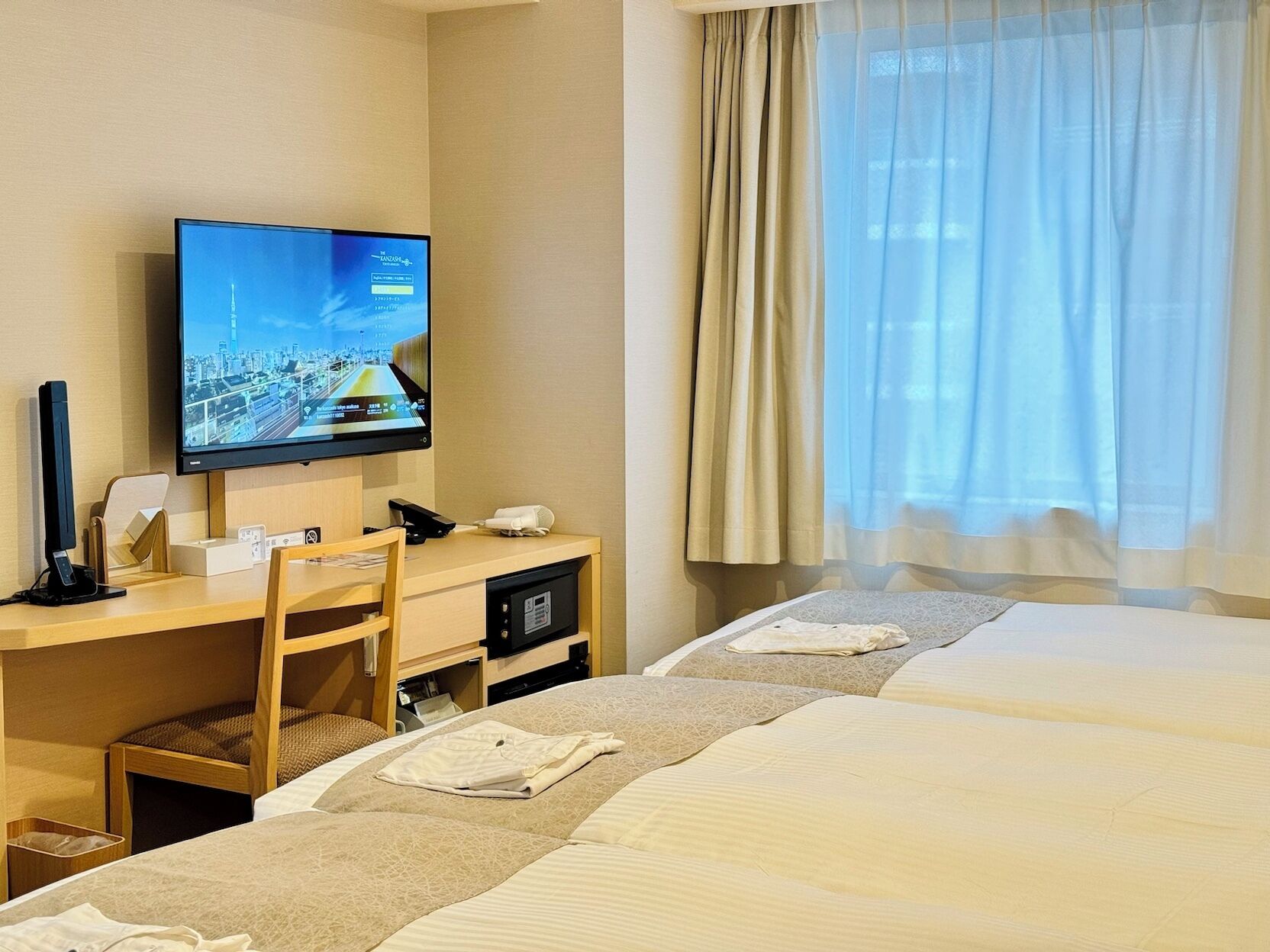 A hotel room with a desk, television, and two beds.