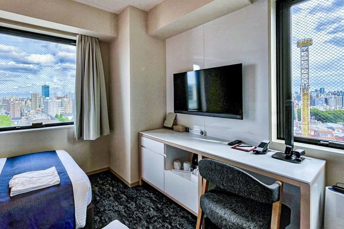 Hotelkamer met een bed, een bureau, een stoel, een televisie en een raam met uitzicht op de stad.