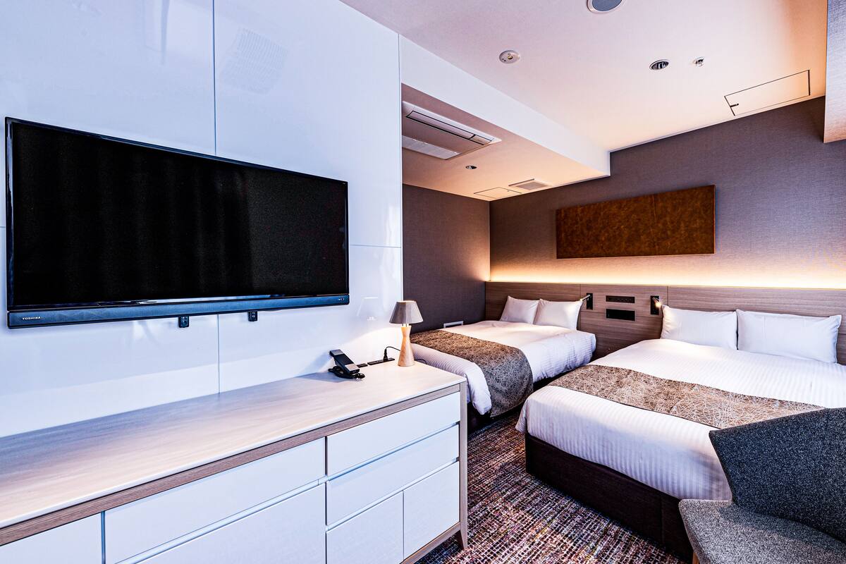 Een moderne hotelkamer met een flatscreen-tv, twee bedden, een bureau met lamp en een groot kunstwerk aan de muur.