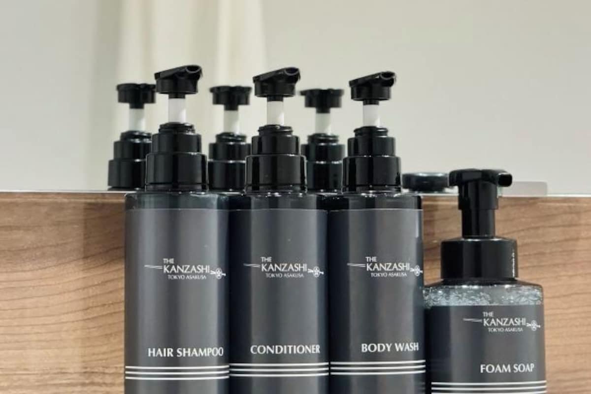 A set of black bottles labeled 'The Kanzashi Tokyo Asakusa' with pump dispensers, including 'Hair Shampoo,' 'Conditioner,' 'Body Wash,' and 'Foam Soap.'