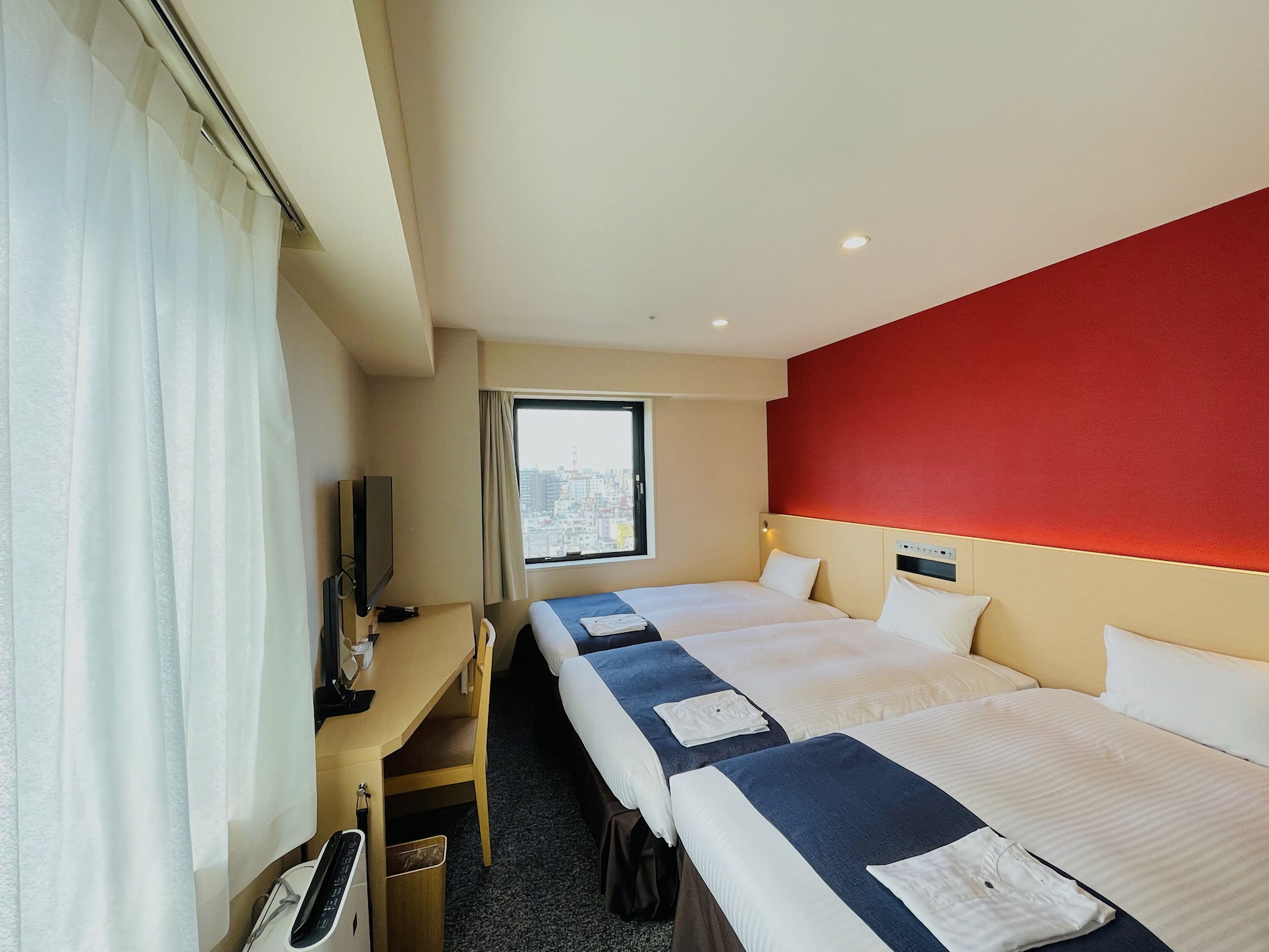 Habitación de hotel con dos camas, un escritorio, un televisor y una ventana con vistas a la ciudad.