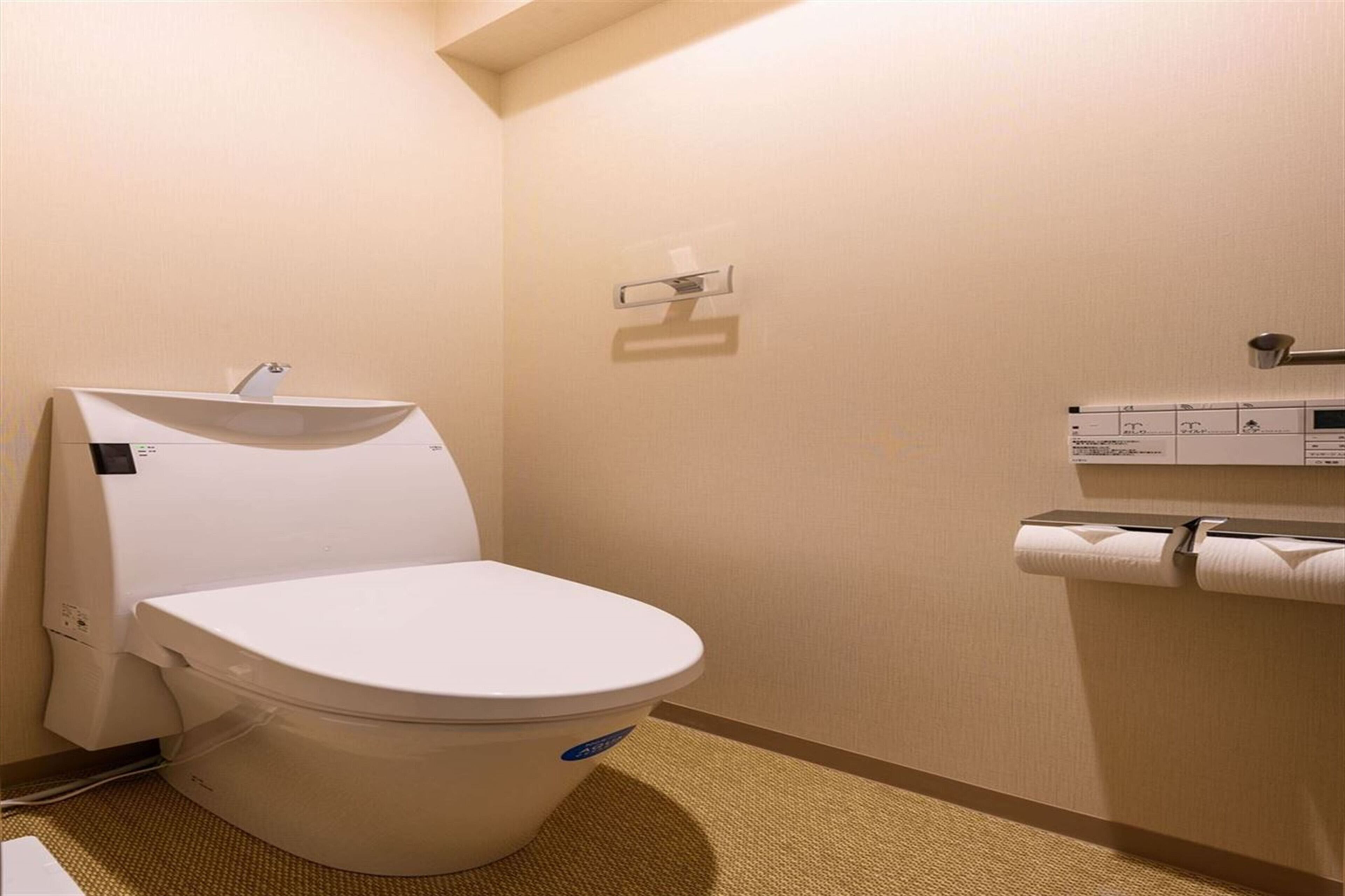 Ein kleines, sauberes Badezimmer mit Toilette, Papierhandtuchspender und einem an der Wand befestigten Toilettenpapierhalter.