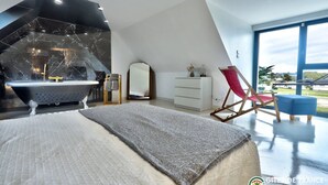 Une chambre à coucher moderne avec un grand lit, une baignoire, une commode blanche et un fauteuil rouge.