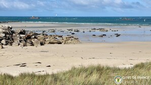 Une plage parsemée de rochers, avec un phare visible au loin.