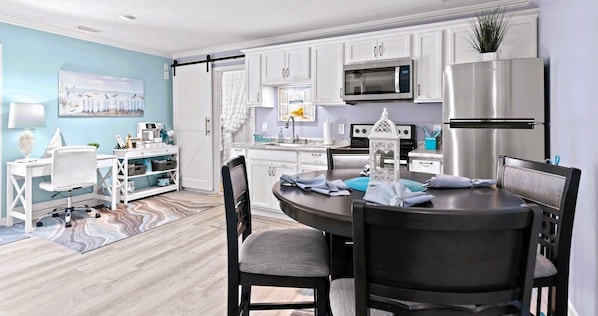 Una cocina moderna con armarios blancos, un microondas, un refrigerador y un comedor con una mesa redonda y sillas.