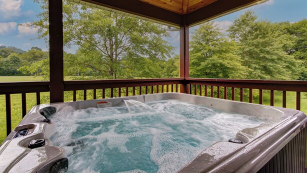 A hot tub with a wooden deck and a view of a green landscape. - Easy Access • No Steep Roads • Near Parkway • Hot Tub • Arcade • 3 Master Suites (Pigeon Forge)