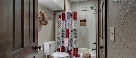 A bathroom with a toilet, shower curtain, and a towel hanging on the wall.