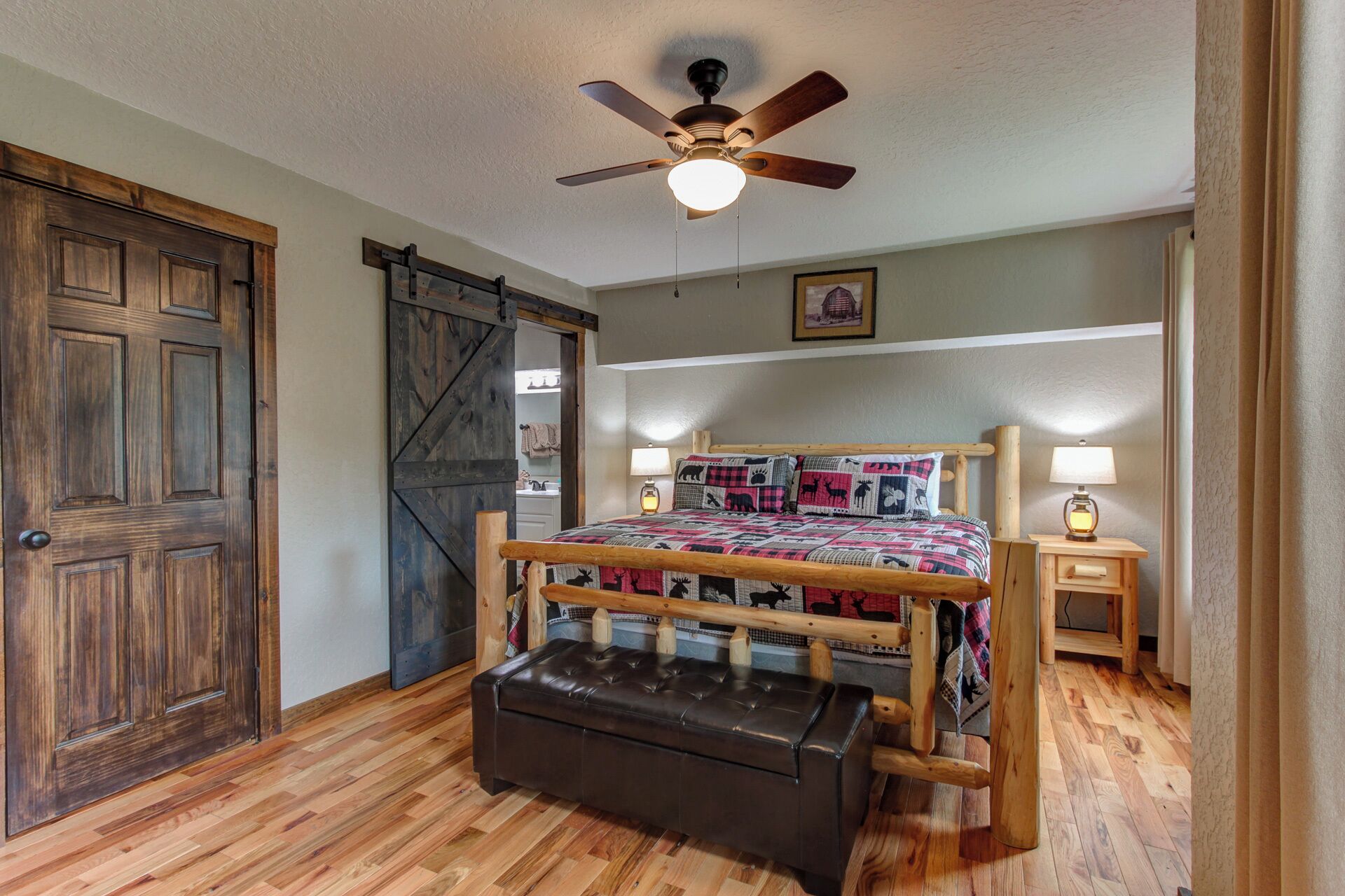 A bedroom with a wooden bed, a ceiling fan, a bench, and a sliding barn door.