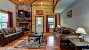 A cozy living room with two sofas, a coffee table, a fireplace, and a television mounted above it. - Easy Access • No Steep Roads • Near Parkway • Hot Tub • Arcade • 3 Master Suites (Pigeon Forge)