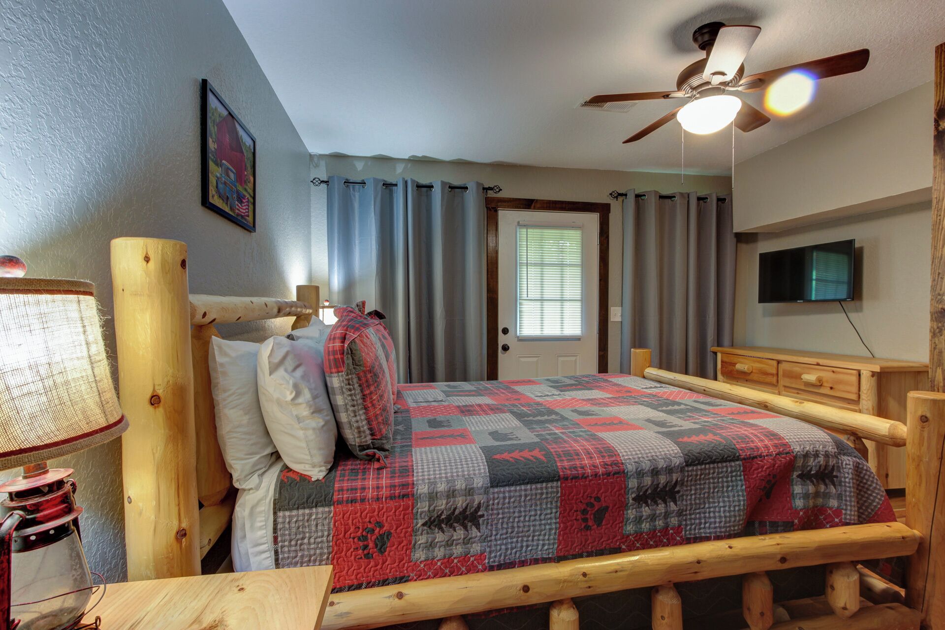 A bedroom with a wooden bed, a ceiling fan, a window with curtains, a television, and a lamp.